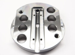 Close-up of a circular metal component with multiple round holes and a central groove against a white background.