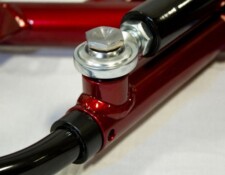 Close-up of a metallic component assembly featuring a red-painted part connected to a black cylindrical piece, secured with a silver bolt and washer.