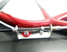 Close-up of a red metal frame with a spring-loaded cable tensioner attached to it, mounted on a black surface.