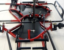A close-up view of the underside of a red and black go-kart chassis showing various components including the frame, steering rods, and mounts.