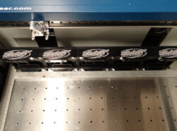 Close-up view of five black objects with engraved logos arranged in a row on an industrial machine bed.